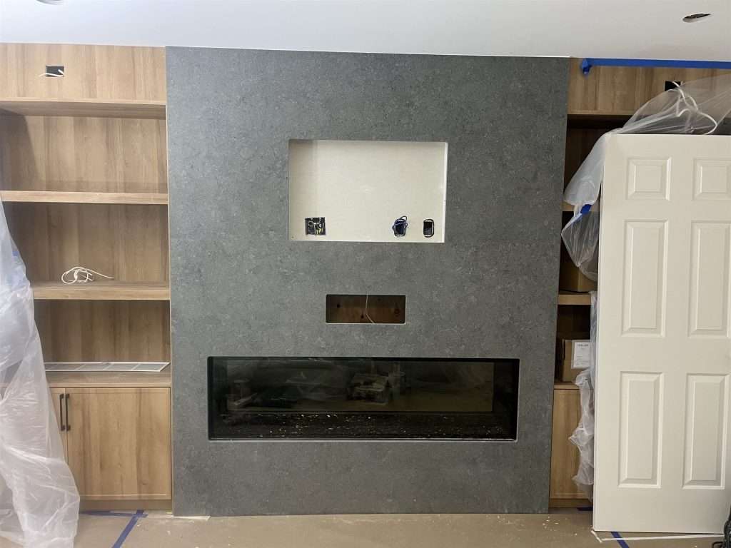 Front view of a matte Dekton Grafite fireplace surround beside wood cabinetry in Langley
